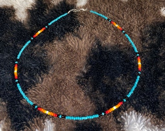 May include: A turquoise, black, orange, red and white beaded necklace. The necklace is made of small, round beads and is strung on a silver chain.