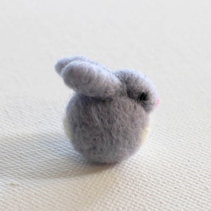 May include: A small, gray felt bunny with a white tail and pink nose.