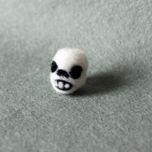 May include: A white felt skull with black eyes and a mouth, resembling a cartoon character.