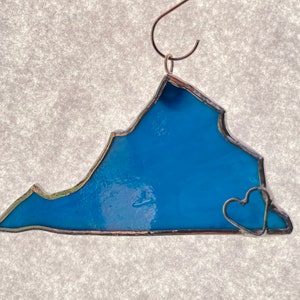 May include: A blue stained glass ornament shaped like the state of Virginia with two small hearts at the bottom.