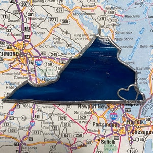 May include: A stained glass depiction of the state of Virginia, outlined in silver, with a heart-shaped cutout at the bottom. The glass is a deep blue color.