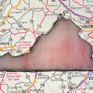 May include: A stained glass depiction of the state of Virginia, outlined in silver, with a pink and white background. The glass is set against a map of Virginia, with various cities and towns labeled.