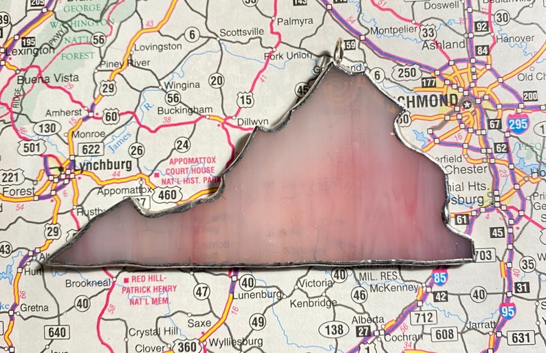 May include: A stained glass depiction of the state of Virginia, outlined in silver, with a pink and white background. The glass is set against a map of Virginia, with various cities and towns labeled.