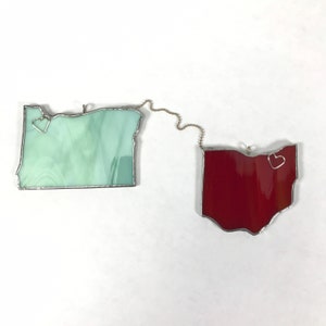 May include: Two stained glass state outlines, Oregon and Ohio, are connected by a silver chain. Each state has a small silver heart in the center.