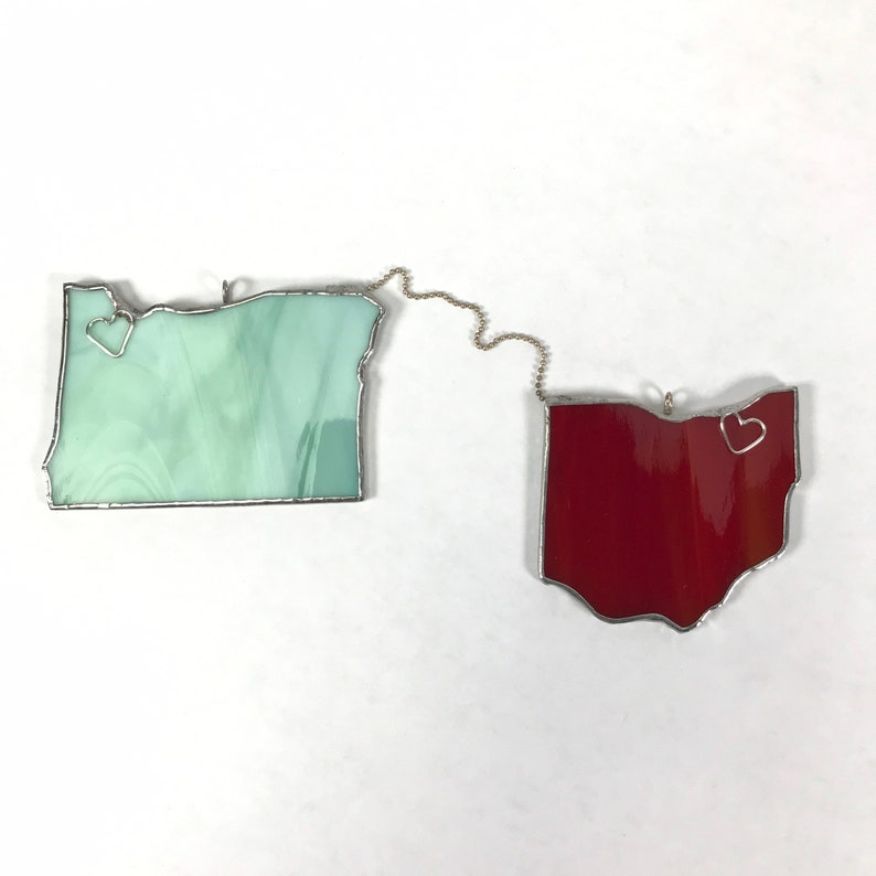 May include: Two stained glass state outlines, Oregon and Ohio, are connected by a silver chain. Each state has a small silver heart in the center.
