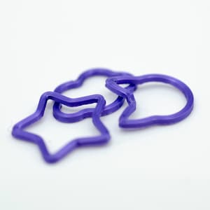 Pode incluir: Três anéis de plástico roxo em forma de estrela, nuvem e balão de fala.