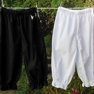 May include: Two pairs of cotton bloomers hanging on a clothesline. One pair is black and the other is white. Both pairs have elastic waistbands and ruffles at the bottom.