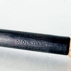 Puede incluir: Primer plano de una herramienta de metal oscuro con mango de madera. La parte met&aacute;lica tiene el texto "J. WILSON" y otras marcas. El mango es de color marr&oacute;n claro.