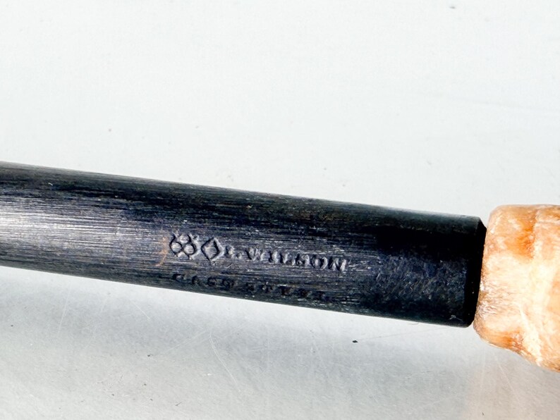 Puede incluir: Primer plano de una herramienta de metal oscuro con mango de madera. La parte met&aacute;lica tiene el texto "J. WILSON" y otras marcas. El mango es de color marr&oacute;n claro.