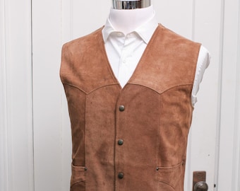 May include: A brown suede vest with a V-neck and four button closure. The vest has two front pockets and is displayed on a mannequin over a white dress shirt. The vest is a medium brown colour.