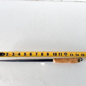 Puede incluir: Un afilador de cuchillos de acero negro con un mango de madera marr&oacute;n claro. El afilador mide aproximadamente 40 cm de largo. Una cinta m&eacute;trica amarilla est&aacute; al lado del afilador.