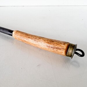 Puede incluir: Un atizador de metal negro con un mango de madera marr&oacute;n claro. El mango tiene una tapa de metal color lat&oacute;n y un lazo de metal negro en el extremo. El atizador est&aacute; dise&ntilde;ado para usar con una chimenea o fogata.