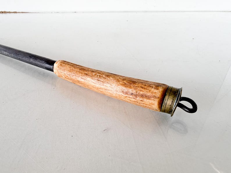 Puede incluir: Un atizador de metal negro con un mango de madera marr&oacute;n claro. El mango tiene una tapa de metal color lat&oacute;n y un lazo de metal negro en el extremo. El atizador est&aacute; dise&ntilde;ado para usar con una chimenea o fogata.