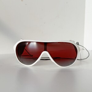 May include: White aviator sunglasses with red tinted lenses. The sunglasses have a white frame and a black strap.