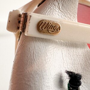May include: Close-up of a white pair of sunglasses with a gold-colored "Wings" logo on the arm.