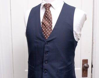May include: A navy blue vest with five buttons and two pockets. The vest is worn over a white shirt with a brown polka dot tie.
