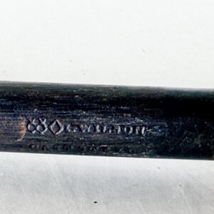 Puede incluir: Primer plano de un mango de madera oscura con el texto en relieve "880-Wellington". El mango es negro con un extremo de color claro. El texto es de estilo vintage.