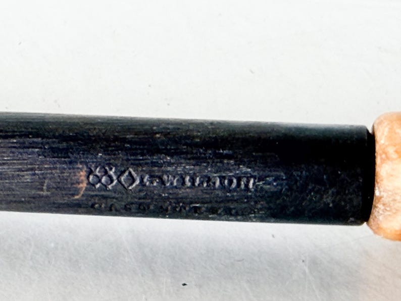 Puede incluir: Primer plano de un mango de madera oscura con el texto en relieve "880-Wellington". El mango es negro con un extremo de color claro. El texto es de estilo vintage.
