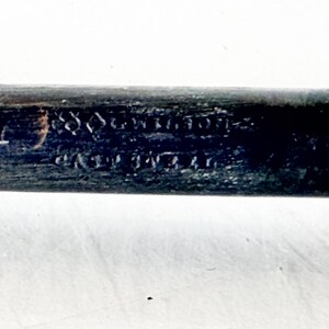 Puede incluir: Primer plano de un mango de madera oscura con texto visible. El mango es negro con un extremo de color claro. El texto parece ser una inscripci&oacute;n, posiblemente una marca del fabricante o informaci&oacute;n de patente.
