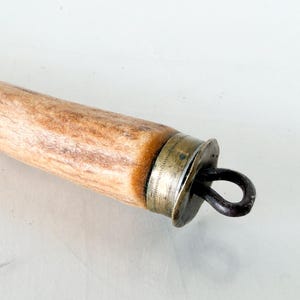 Puede incluir: Primer plano de un mango de madera con una tapa de metal y un lazo de metal oscuro. El mango es de color marr&oacute;n claro con vetas m&aacute;s oscuras. La tapa de metal es plateada y tiene un dise&ntilde;o decorativo.