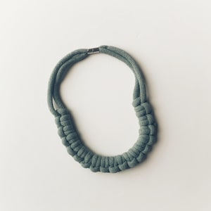 May include: A sage green knotted rope necklace with a silver clasp.