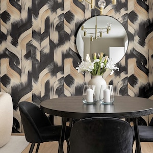 May include: A dining room with a dark wood table and four black velvet chairs. A white vase with white flowers and two glass candle holders are on the table. A round mirror hangs on the wall, and a gold chandelier is above the table. The wallpaper has a black and beige pattern.