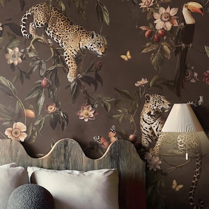May include: A bedroom with a dark brown floral wallpaper depicting leopards, toucans, and butterflies. A wooden headboard with a wavy design is in front of the wallpaper. The bed has grey pillows and a round, textured decorative pillow.