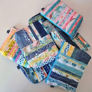May include: A collection of colorful patchwork fabric zipper pouches with denim accents. The pouches are made with a variety of fabrics, including stripes, polka dots, and floral patterns. The pouches are all different sizes and shapes.