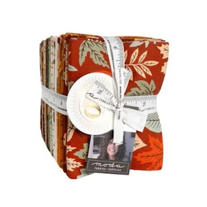 May include: A stack of folded fabric squares featuring a rust-orange background with a pattern of autumn leaves in cream and sage green. The stack is secured with a white measuring tape marked in inches and a tag labeled Moda Fabrics Supplies.