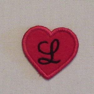 May include: Red felt heart with a black embroidered letter L.