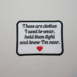 May include: White embroidered patch with black text that reads "These are clothes I used to wear, hold them tight and know I'm near." A red heart is embroidered below the text.