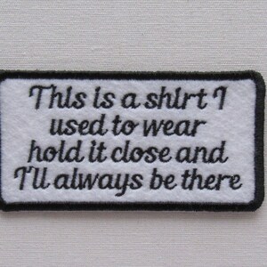 May include: White embroidered patch with black stitching and the text "This is a shirt I used to wear hold it close and I'll always be there."