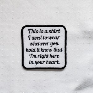 May include: A white embroidered patch with black stitching. The patch features the text "This is a shirt I used to wear whenever you hold it know that I'm right here in your heart."