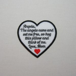 May include: White heart-shaped embroidered patch with black text that reads "Angela, The angels came and set me free, so hug this pillow and think of me. Love, Mom". A small red heart is embroidered at the bottom of the patch.