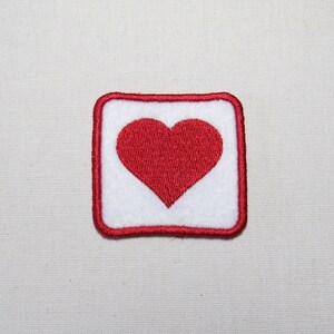May include: A red heart embroidered on a white square patch with a red border.