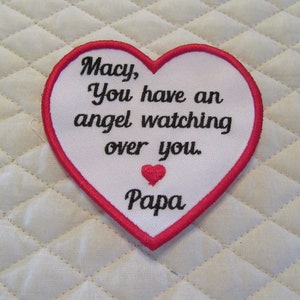 May include: White heart-shaped patch with red stitching. The patch has black embroidered text that reads "Macy, You have an angel watching over you. Papa".