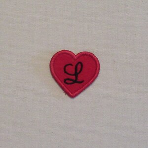 May include: Red felt heart-shaped patch with a black embroidered letter L.