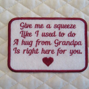 May include: White felt patch with red embroidered border and text. The text reads "Give me a squeeze Like I used to do A hug from Grandpa Is right here for you." A red heart is embroidered below the text.