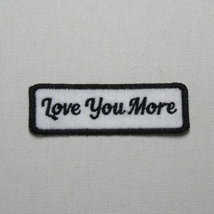 May include: White embroidered patch with black stitching and the text "Love You More" in a cursive font.