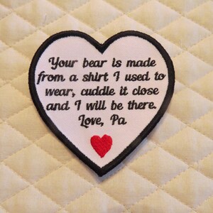 May include: White heart-shaped patch with black stitching and a red heart in the center. The patch has the text "Your bear is made from a shirt I used to wear, cuddle it close and I will be there. Love, Pa."