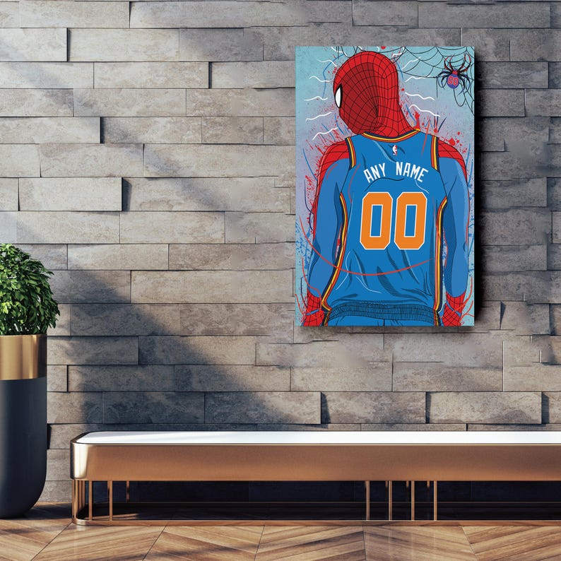 Op de afbeelding: Een blauw en oranje basketbaltenue met de tekst "ANY NAME" en het nummer "00" op de rug. Het tenue wordt gedragen door een Spiderman-personage met een rood en blauw pak. De achtergrond is een blauw en wit abstract ontwerp met een spinnenweb.