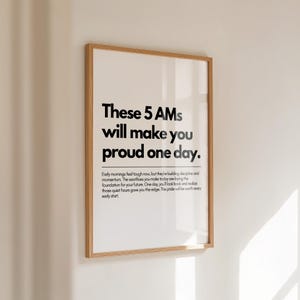 Pu&ograve; includere: Una stampa incorniciata con la scritta "These 5 AMs will make you proud one day." La stampa ha uno sfondo bianco con testo nero e una cornice in legno. Il testo descrive i benefici delle prime ore del mattino.