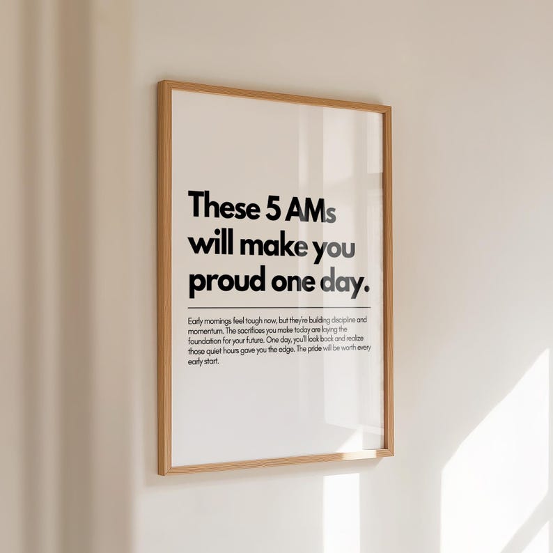 Pu&ograve; includere: Una stampa incorniciata con la scritta "These 5 AMs will make you proud one day." La stampa ha uno sfondo bianco con testo nero e una cornice in legno. Il testo descrive i benefici delle prime ore del mattino.