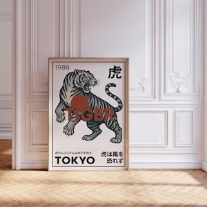 May include: Framed art print featuring a detailed illustration of a tiger with black stripes, a red circle, and the word "TIGER". The print includes Japanese text and the word "TOKYO". The artwork is displayed in a room with white walls and a wooden floor.