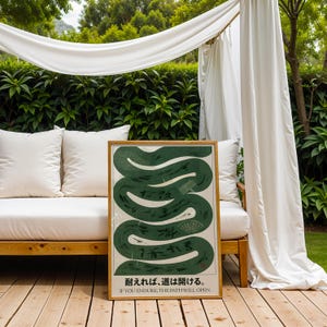May include: A framed art print featuring a stylized green snake design with Japanese text and the English phrase "IF YOU ENDURE, THE PATH WILL OPEN." The artwork has a cream-colored background and a wooden frame, displayed outdoors.