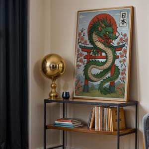May include: A framed art print featuring a green dragon with a red sun and Japanese text. The artwork is displayed on a dark wood and metal console table, alongside a gold sphere lamp and a stack of books.