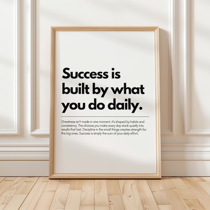 May include: A framed print with the text "Success is built by what you do daily." The print is in a light wood frame and is displayed against a white wall. The text is in a bold, black font.