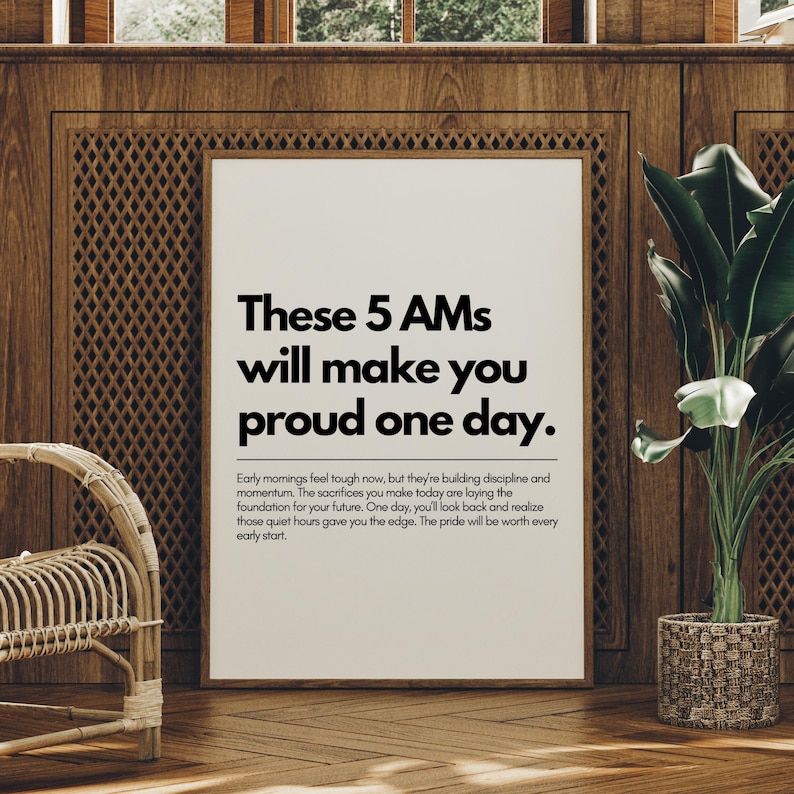 Pu&ograve; includere: Una stampa incorniciata con il testo "These 5 AMs will make you proud one day." La stampa &egrave; esposta in una stanza con pannelli di legno, una sedia in vimini e una pianta in vaso. Il testo &egrave; nero.