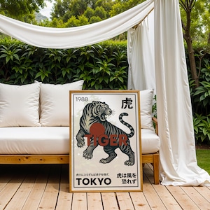 May include: A framed poster featuring a black and gray tiger illustration with the word "TIGER" in red. The poster includes Japanese text and the year "1988". The artwork is displayed outdoors, leaning against a white couch.