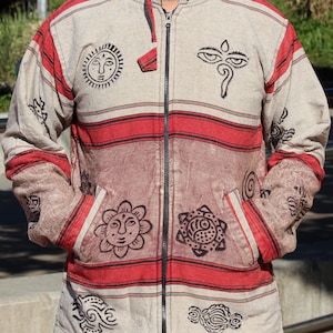 May include: A beige and red striped jacket with a zipper closure. The jacket has black and white printed designs of suns, eyes, and swirls.